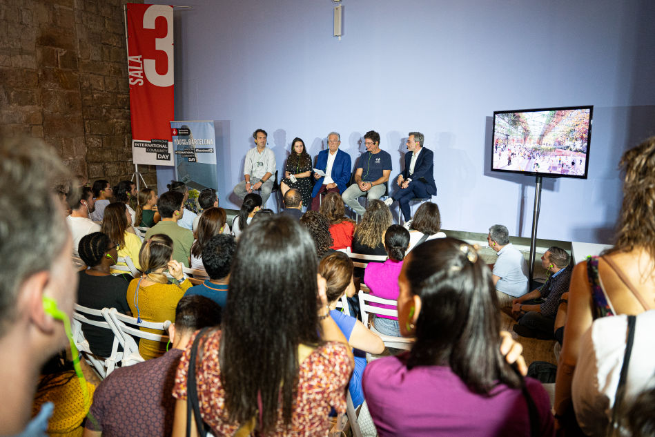 Photograph of a crowd of people listening to a panel of speakers at Barcelona International Community Day 